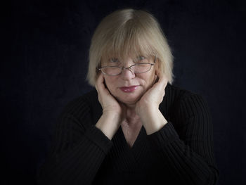 Portrait of mature woman with hands on cheeks against black background