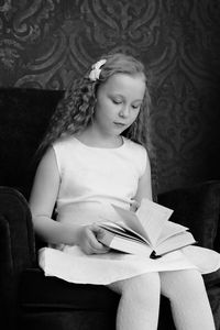 Girl reading book while sitting on chair