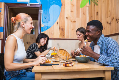 Positive young multiracial friends eating tasty dishes and burgers while gathering in modern restaurant