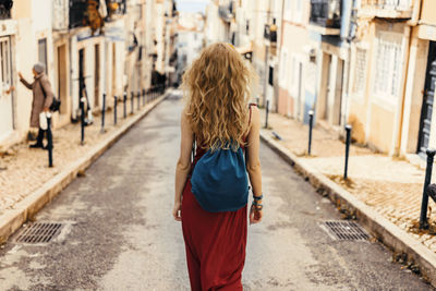 Rear view of woman with backpack walking on road amidst buildings