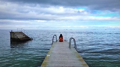 Rear view of woman sitting on pier over sea