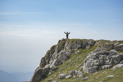 Man on rock by mountain against sky