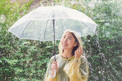 Woman with umbrella standing against trees during rainy season