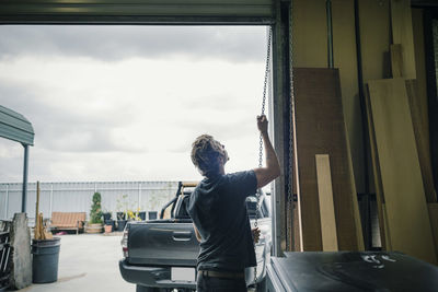 Rear view of carpenter pulling shutter at entrance of workshop