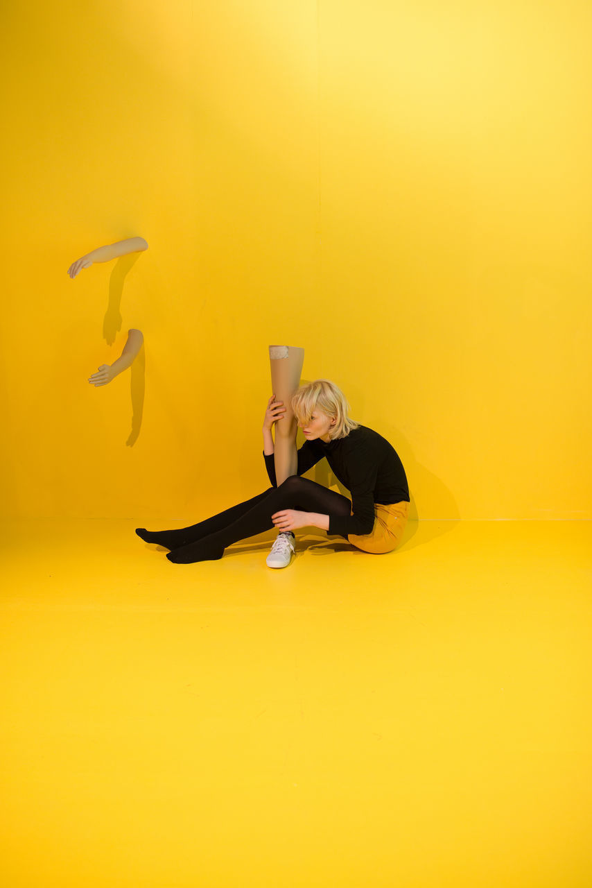 Woman holding mannequin leg while sitting over yellow background