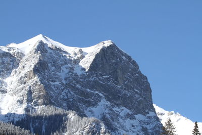 Low angle view of snowcapped mountains against clear blue sky