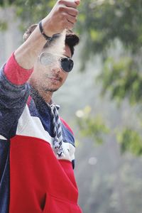 Portrait of young man wearing sunglasses throwing sand outdoors