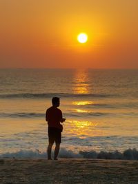 Rear view of man standing on beach during sunset
