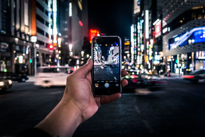 Cropped image of hand holding smart phone on city street