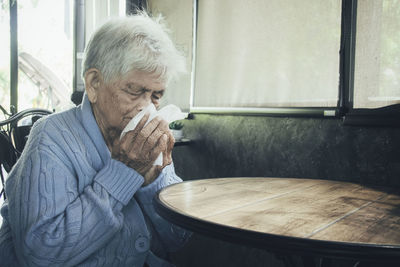 Old person coughing covering mouth with a tissue on a house interior. she has flu, allergy symptoms.