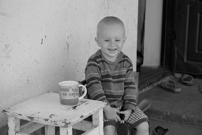 Boy smiling while sitting at table against wall