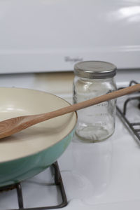 Close up of a clean frying pan with a wooden spoon in it and an empty glass jar next to it