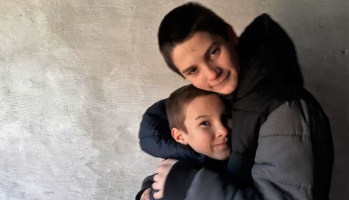 Portrait of boy embracing brother while wearing warm clothing by wall