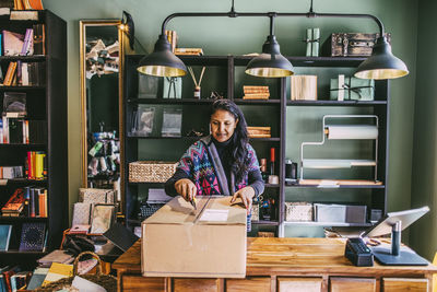Female shop owner opening cardboard box at checkout in store