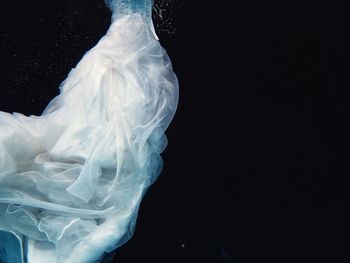Close-up of wedding dress under water against black background