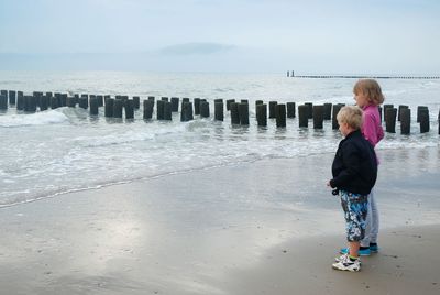 Side view of siblings standing at beach against sky