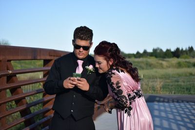 Smiling couple looking at smart phone while standing against clear sky