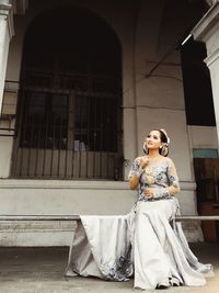 Woman sitting on rod against building