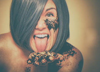 Close-up portrait of shirtless messy woman sticking out tongue against beige background