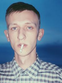 Portrait of young man smoking cigarette against blue sky