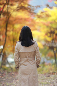 Rear view of woman standing against trees during autumn