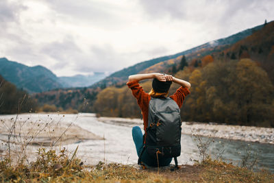 Rear view of man sitting on mountain against sky