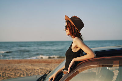 Young woman wearing hat on beach against sky