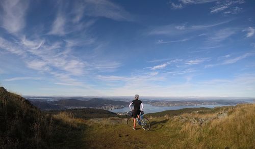 Rear view of man with bicycle standing on mountain against sky