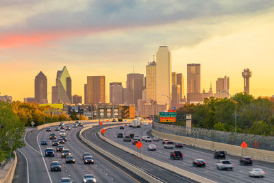 Cars on road amidst buildings in city against sky during sunset