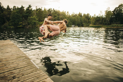 Playful male friends jumping together in lake during vacation