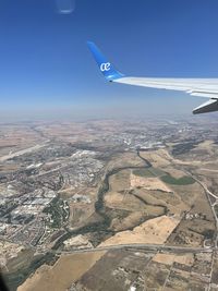 Aerial view of airplane flying over landscape against blue sky