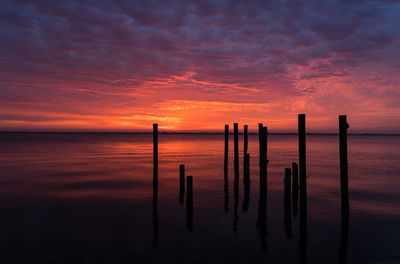 Wooden posts in sea against sunset sky