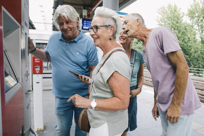 Group of senior friends buying ticket on railway station platform