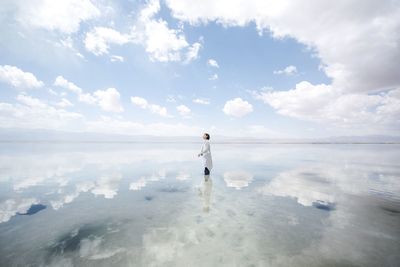 Reflection of cloudy sky and woman on sea