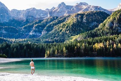 Rear view of shirtless man standing by lake against mountain