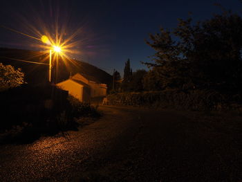 Road amidst trees and buildings against sky during sunset