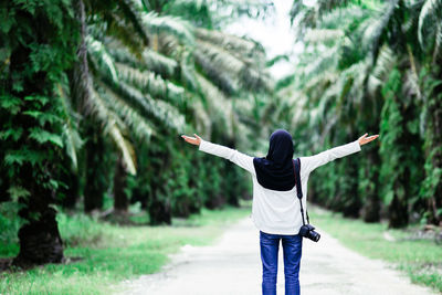Rear view of woman with arms outstretched against trees in forest