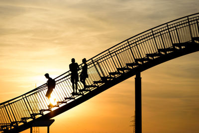 Silhouette people on footbridge against sky