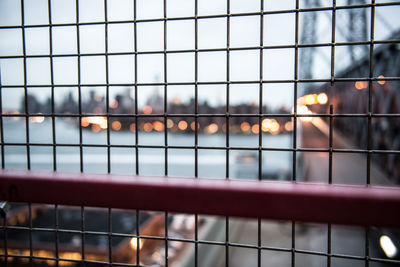 Full frame shot of illuminated fence and waterway against city skyline during sunset