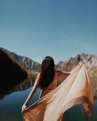 Rear view of woman holding umbrella against clear blue sky