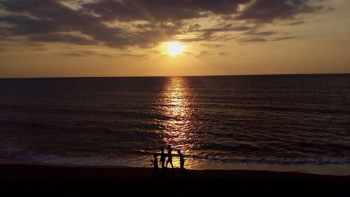 Silhouette people on shore at beach against sky during sunset