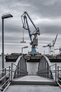 Cranes at harbor against cloudy sky