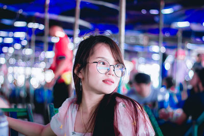 Smiling young woman wearing eyeglasses looking away while standing outdoors at night