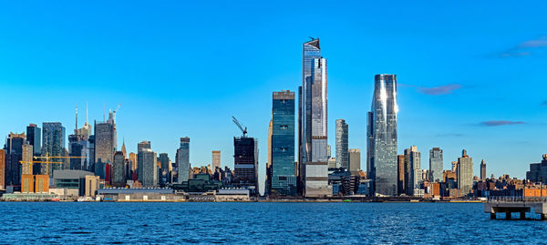 Sea by modern buildings against blue sky