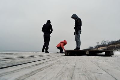 Family standing on pier at beach against clear sky