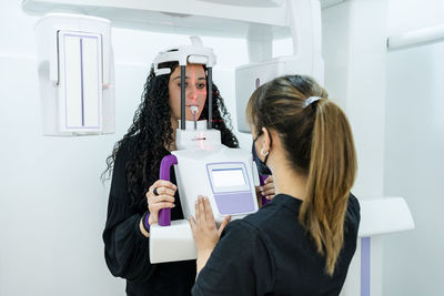 Female dentist operating machine during medical examination of young patient at clinic