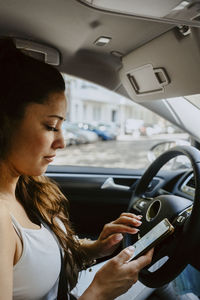 Mid adult woman using map on mobile phone while sitting in electric car