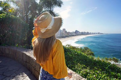 Woman with straw hat and raglan shirt with leblon and ipanema beaches on background, rio de janeiro