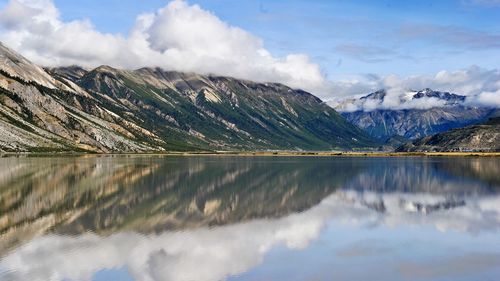 Scenic view of lake by mountains against cloudy sky