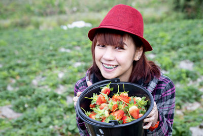 Portrait of a smiling young woman holding strawberry outdoors